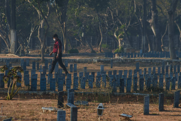 Funcionário caminha entre sepulturas do cemitério Parque Bom Jardim, que viu demanda por enterros crescer na pandemia de Covid-19 em Fortaleza (CE)  