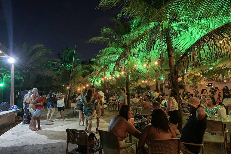 Casais dançam forró ao ar livre ao lado de pessoas sentadas em barraca da Praia do Futuro, em Fortaleza (CE)