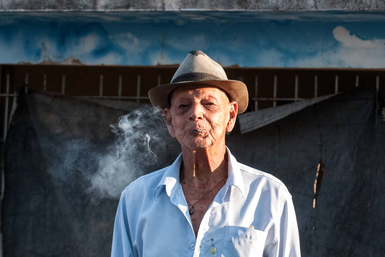 Homem idoso de camisa branca e chapéu fumando