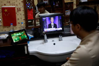 Barber watches a video on a pad next to a screen showing Democratic 2020 U.S. presidential nominee Joe Biden delivering a speech after the news media announced that he has won the 2020 U.S. presidential election, at the Jin Ban Cun barbershop in Beijing
