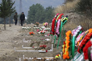 FILE PHOTO: Men walk along graves of soldiers and civilians who were killed during a military conflict over the breakaway region of Nagorno-Karabakh, in Stepanakert