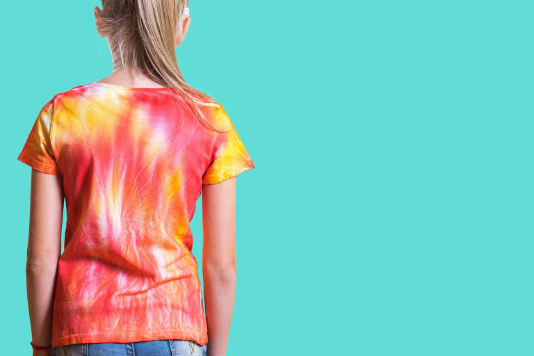 View from the back of a girl in a t-shirt in the style of tie dye on a turquoise background.