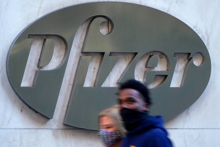 Casal caminha diante de logotipo de prédio da Pfizer, em Nova York, nos Estados Unidos