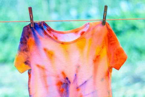 T-shirt painted in tie dye style is dried on a rope. White clothes painted by hand.