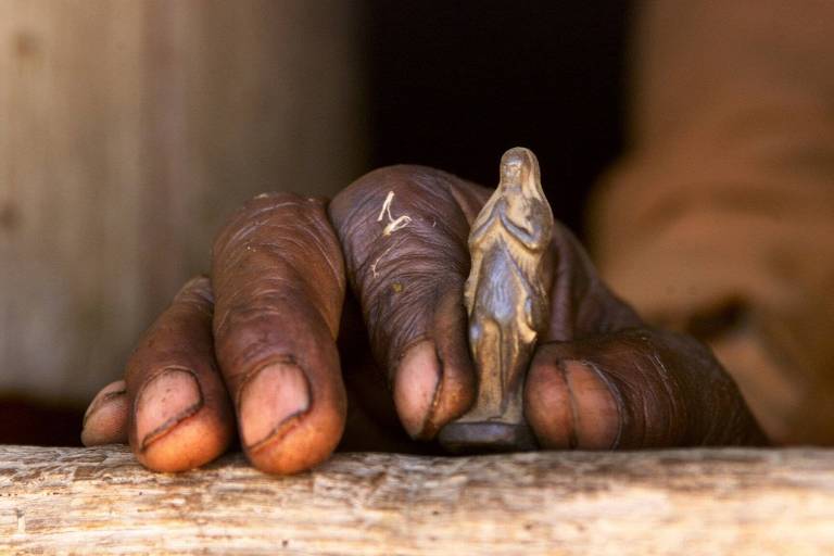mão de pessoa negra idosa segura miniatura dourada de um santo 