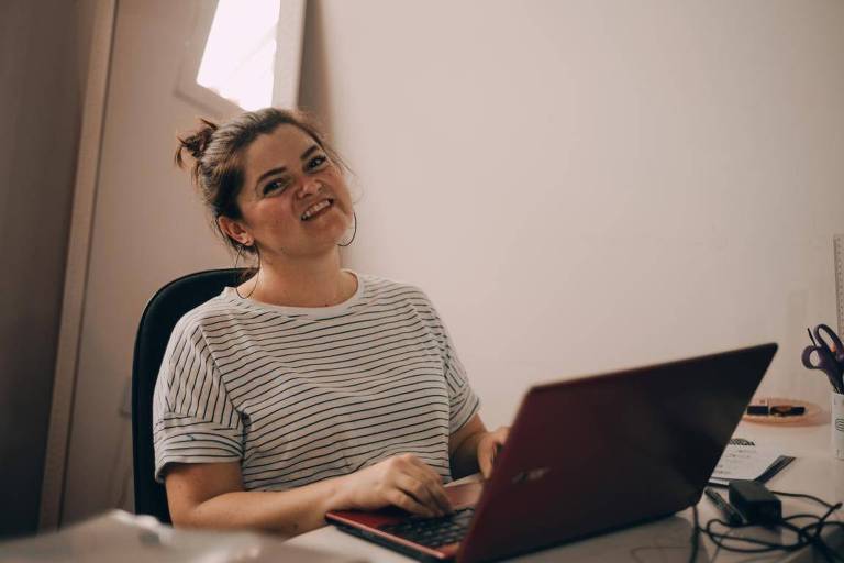 Empresária usa blusa listrada e sorri em frente ao laptop