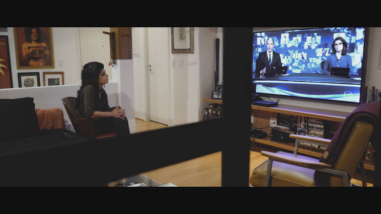 Cena do documentário 'Cercados' mostra repórter do 'Profissão Repórter' assistindo ao Jornal Nacional