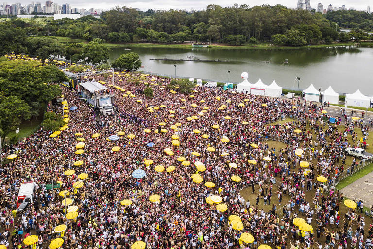 Vista de cima de avenida lotada de pessoas em meio a guarda-sóis amarelos de ambulantes