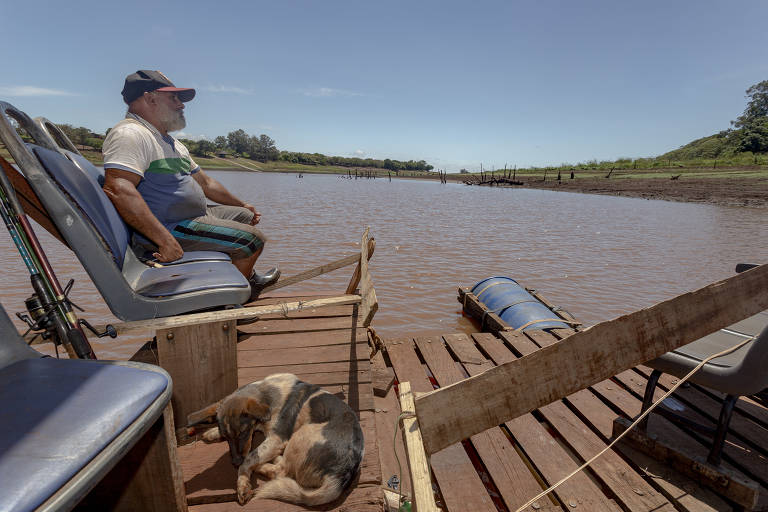 Nicolas Carmona Carmona Nebreira em seu barco pesqueiro, nas margens rachadas onde costuma ser o leito de um dos braços do Rio Tibagi, na Represa de Capivara, região da cidade de Primeiro de Maio.