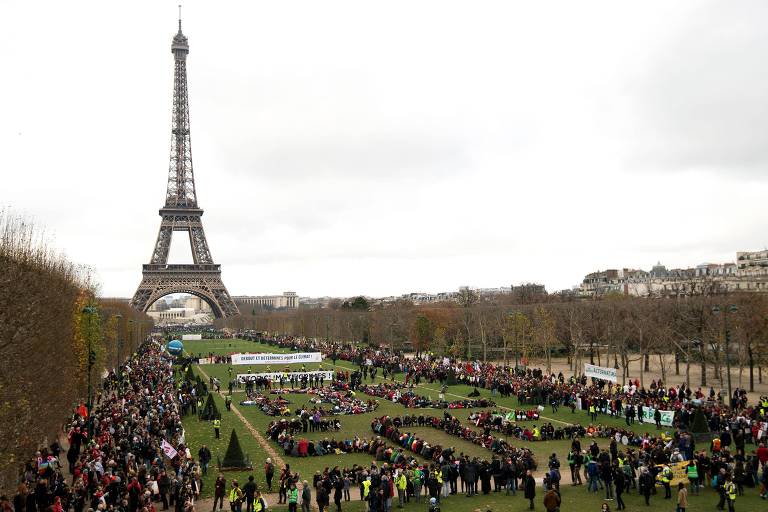 Pessoas reunidas em um gramado verde com a Torre Eiffel ao fundo