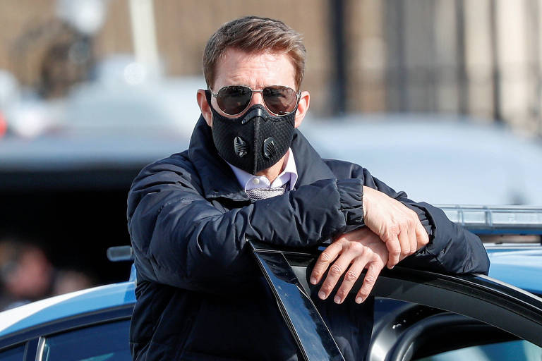 Tom Cruise de máscara apoiado na porta de um carro
