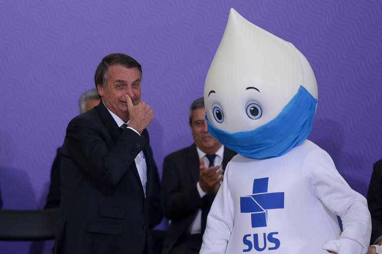 Bolsonaro coloca a mão no nariz em tom jocoso com Zé Gotinha ao seu lado