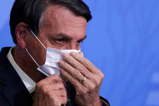 FILE PHOTO: Brazil's President Jair Bolsonaro looks on as he adjusts his protective face mask during a ceremony launching a program to expand access to credit at the Planalto Palace in Brasilia