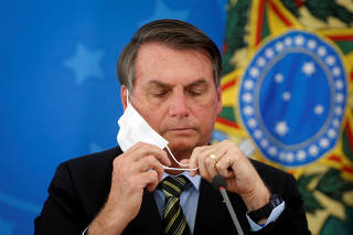 FILE PHOTO: Brazil's President Jair Bolsonaro adjusts his protective face mask during a press statement to announce federal judiciary measures to curb the spread of the coronavirus disease (COVID-19) in Brasilia