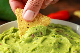 Man hand is picking some guacamole dip with nachos chip. Healthy Vegan, Vegetables food.