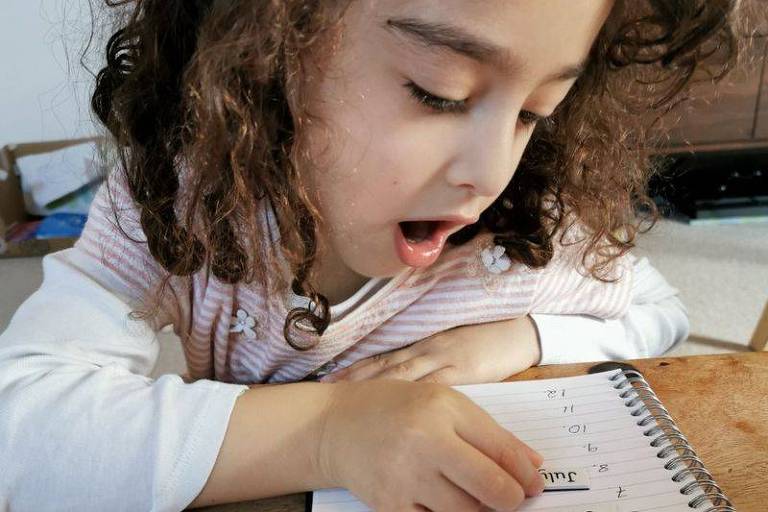 Uma criança coloca um adesivo com uma palavra em um caderno