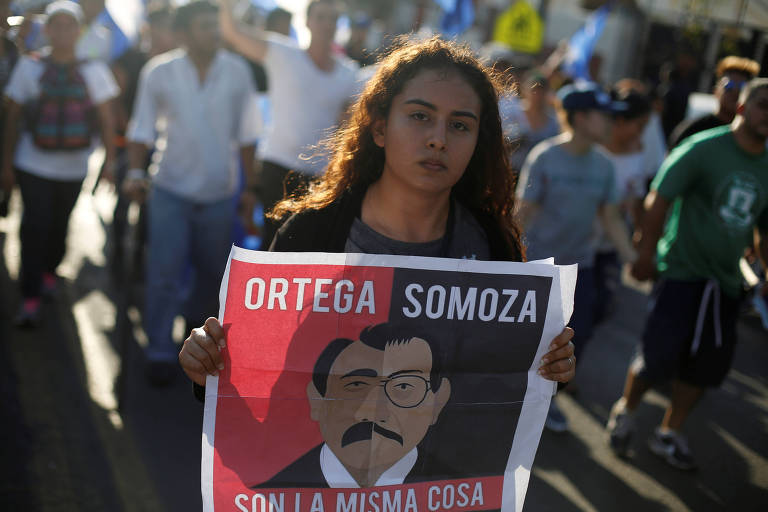 Manifestante segura cartaz comparando o ditador Daniel Ortega ao ditador Anastasio Somoza em protesto contra violência da polícia e o governo de Ortega, em Manágua, em 23 de abril de 2018. 

