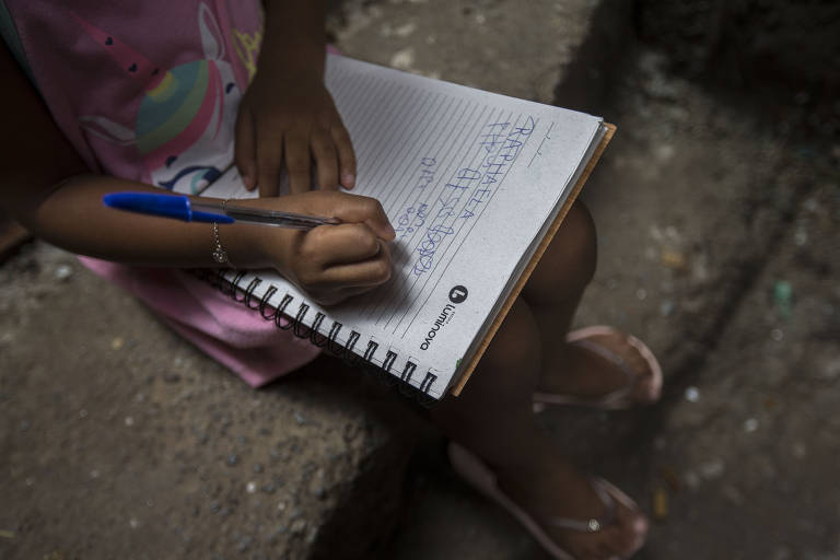 Imagem em close mostra criança escrevendo em um caderno