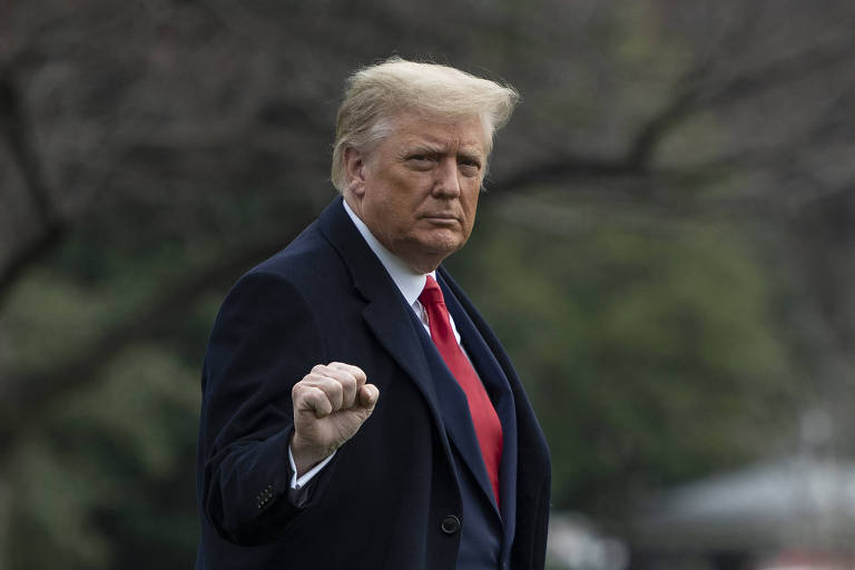 Fotografia colorida mostra Donald Trump com punho erguido; ele é branco, quase laranja, e tem cabelo loiro curto; ele usa  um terno azul marinho e gravata vermelha