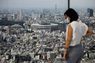 FILE PHOTO: The National Stadium, the main stadium of Tokyo 2020 Olympics and Paralympics, is seen past a visitor wearing a protective face mask amid the coronavirus disease (COVID-19) in Tokyo