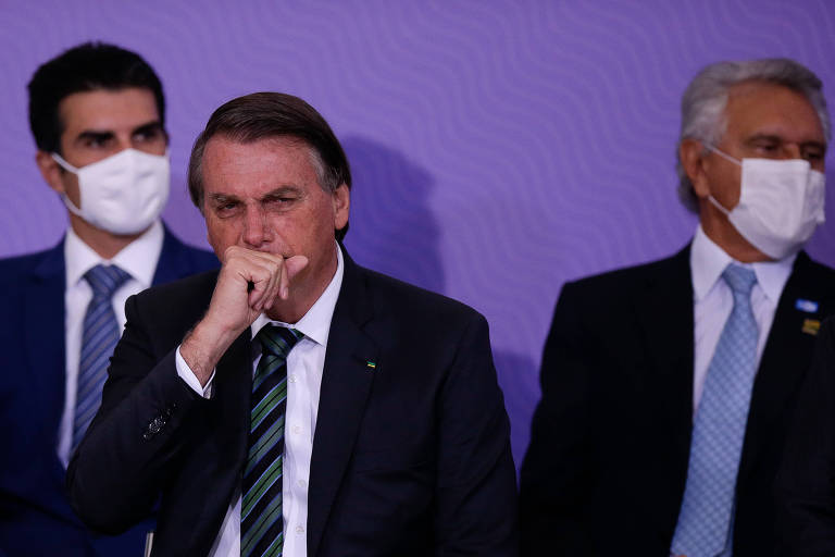 No palco, Bolsonaro coloca a mão na boca ao tossir, sem máscara; ao fundo, governadores usam máscara