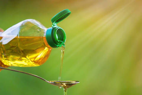 Hand pouring Vegetable oil from bottle to spoon with nature background