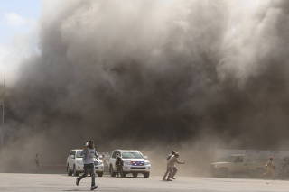 People react as dust rises after explosions hit Aden airport, upon the arrival of the newly-formed Yemeni government in Aden