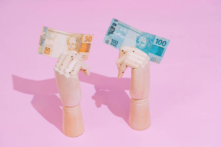 Mãos de plástico seguram notas de R$100 e de R$50