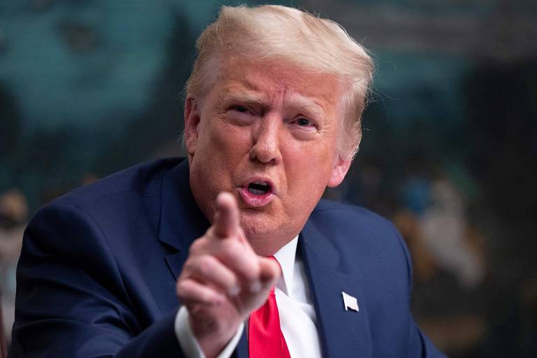 Donald Trump, de paletó azul, camisa branca e gravata vermelha aponta o dedo indicador