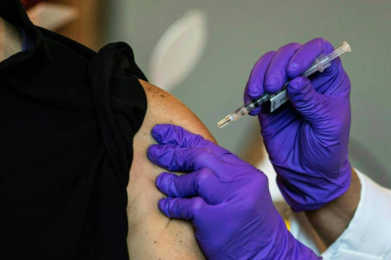 mao com luva roxa aplica injeção em braço de pessoa com camiseta preta