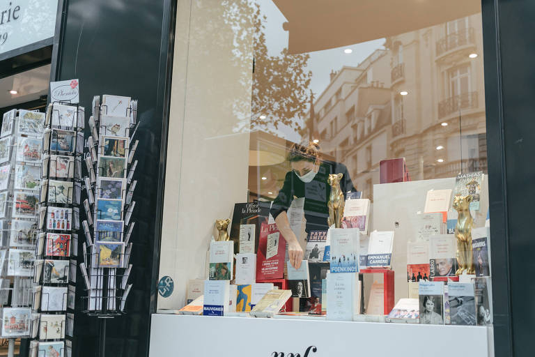 Mulher de máscara ajeita livro em vitrine de livraria na França