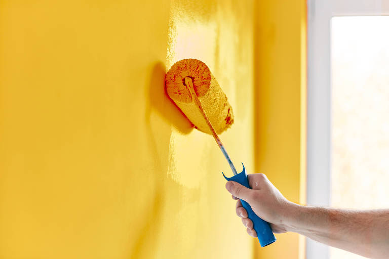 Foto mostra mão de uma pessoa segurando rolo de pintura para pintar uma parede de um imóvel