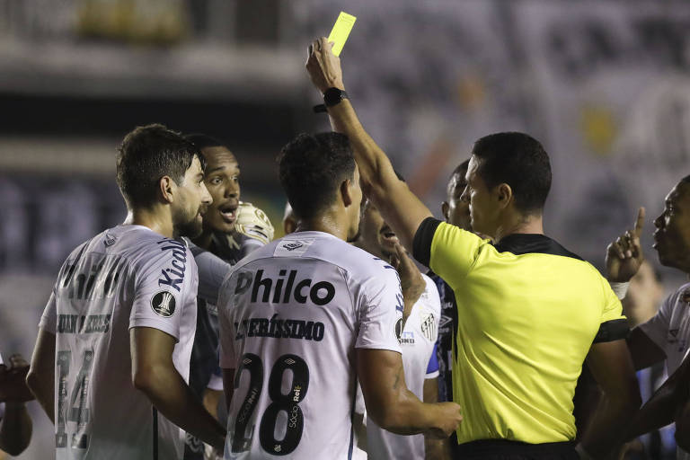 O árbitro colombiano Wilmar Roldán mostra o cartão amarelo para John na partida entre Santos e Grêmio pela Libertadores