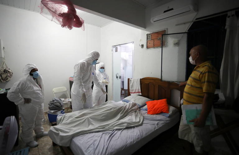 Edvaldo Braga (dir.) observa enquanto trabalhadores municipais de saúde examinam o corpo de sua mãe Lacy Braga de Oliveira, que morreu em casa aos 84 anos, em meio à pandemia, em Manaus