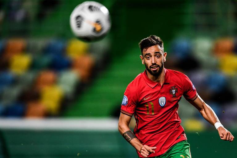 Jogador com uniforme vermelho da seleção portuguesa corre olhando para a bola