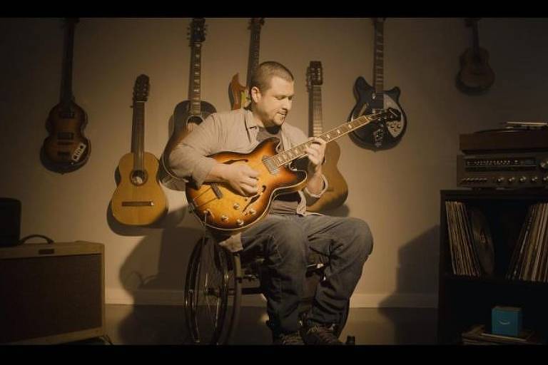 Homem em cadeira de rodas toca guitarra;ele usa dispositivo da Amazon para controlar a iluminação (divulgação)