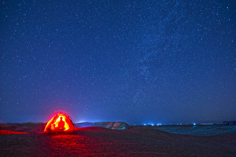 Céu estrelado e uma pessoa (aparentemente) sob uma tenda iluminada