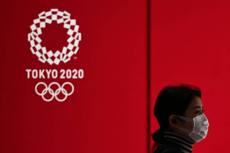 Mulher, de máscara, caminha próxima a display da Olimpíada de Tóquio
