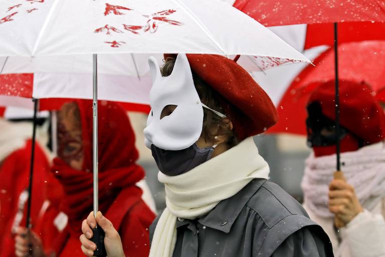 Mulher de máscara branca de gato e máscara contra covid, de boina vermelha e guarda-chuva branco, entre outras também com as cores vermelho e branco