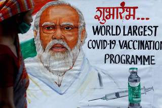 FILE PHOTO: A woman walks past a painting of Indian Prime Minister Narendra Modi a day before the inauguration of the COVID-19 vaccination drive on a street in Mumbai