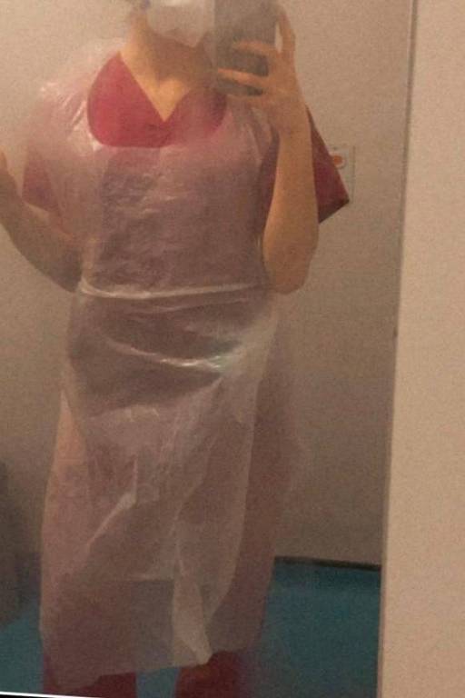 Selfie tirada no espelho mostra moça de uniforme vermelho e avental de plástico que não cobre os braços; o rosto não aparece