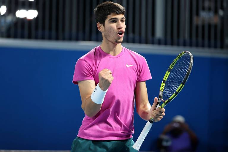 Tenista de camisa rosa vibra com a raquete na mão