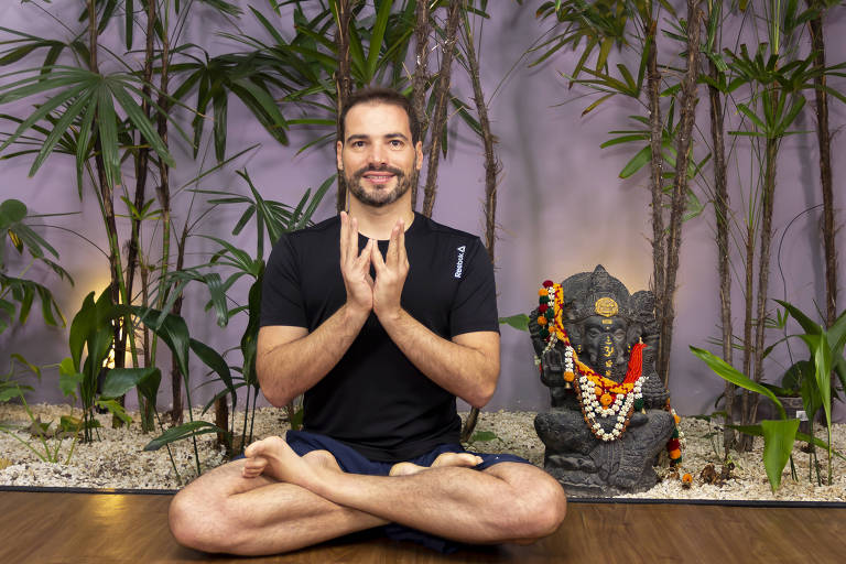 Ricardo Carneiro em pose de ioga no chão com um fundo com plantas