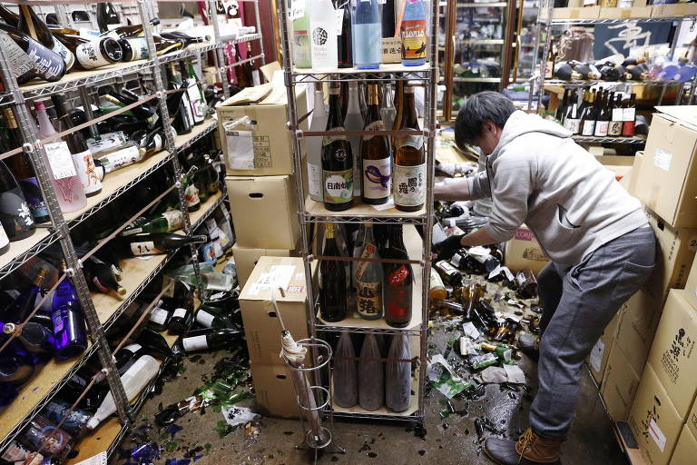 Funcionário de loja de bebidas alcoólicas em Fukushima realiza limpeza após terremoto fazer com que garrafas se quebrassem