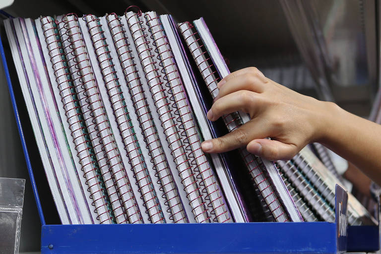 foto mostra mão de pessoa escolhendo cadernos que estão em prateleira 
