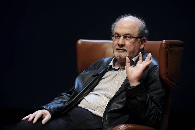 Imagem mostra o autor Salman Rushdie sentado e conversando durante seminário