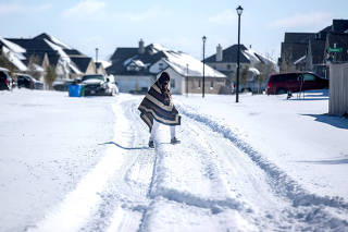 FILE PHOTO: A man walks to his friend's home in a neighbourhood without electricity as snow covers the BlackHawk neighborhood in Pflugerville