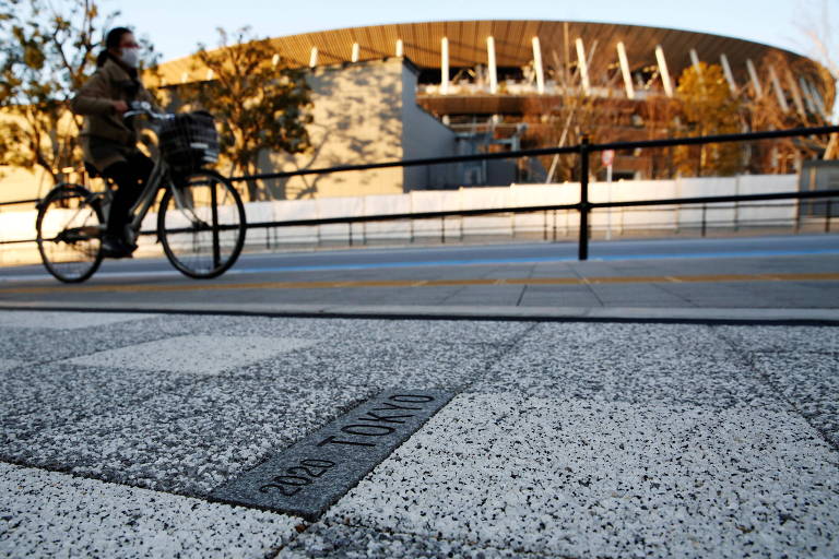 Mulher passeia de bicicleta em frente ao Estádio Nacional de Tóquio, uma das praças esportivas da Olimpíada