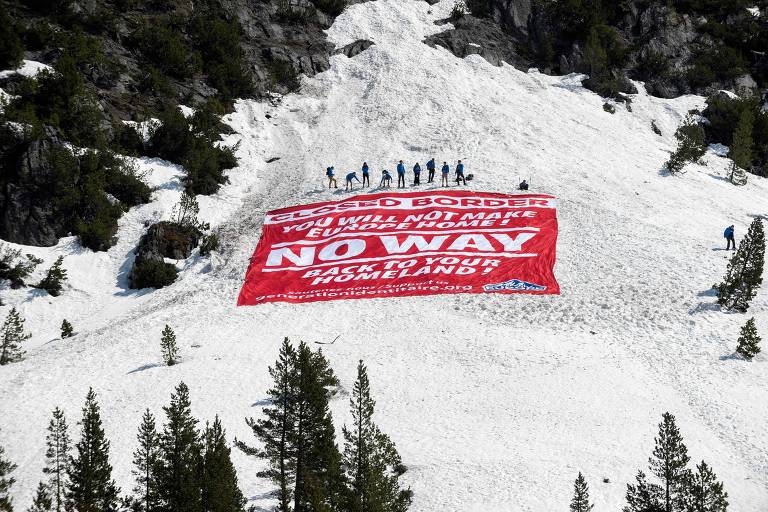 Em morro cheio de neve, dez pessoas estendem grande faixa vermelha com mensagens contra a entrada de imigrantes na França