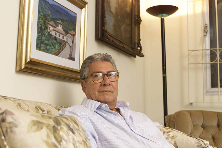 Mário Covas sentado em sofá com quadros ao fundo